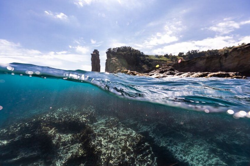 A coastal scene with clear turquoise water, a rocky cliff, and a lighthouse. 3