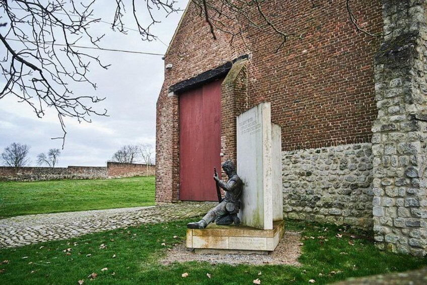A statue of a person sitting on a bench in front of a brick building with a red door. 4