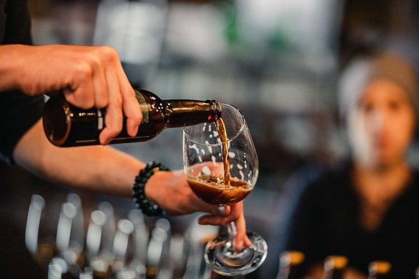 A person pouring a dark liquid from a bottle into a clear glass. 2