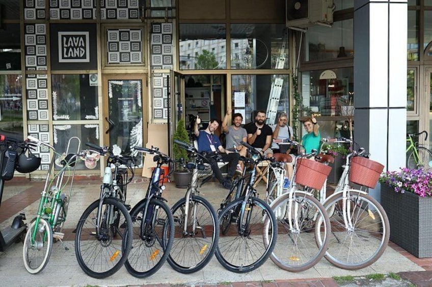 A group of people sitting on a bench outside a store with bicycles parked in front. 1