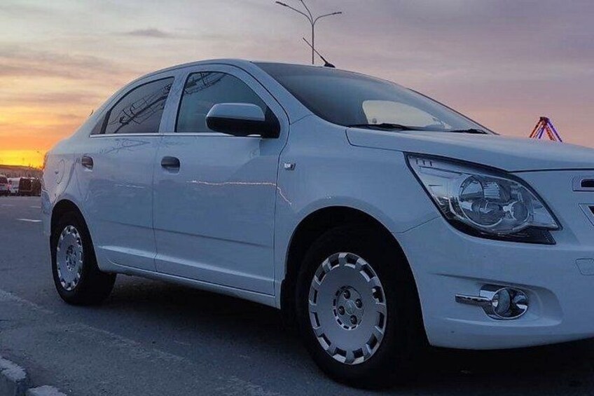 A white sedan parked on a road with a sunset in the background. 5