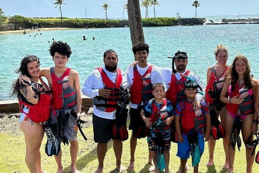 A group of people wearing life jackets by a beach with palm trees and the ocean in the background. 3