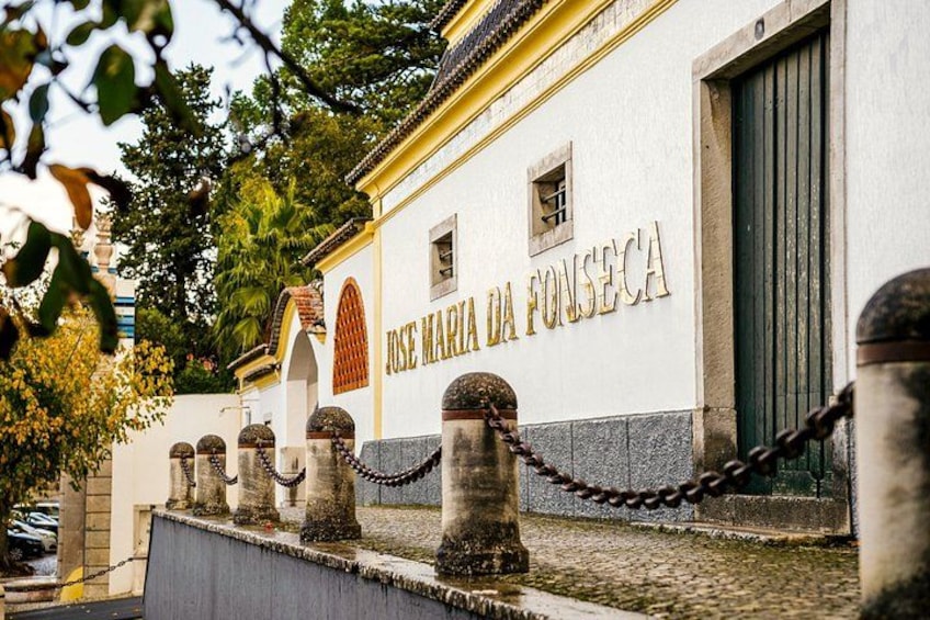 Un edificio con la inscripción 'JOSE MARIA DA FONSECA' y una cerca de malla con pilares de piedra. 2