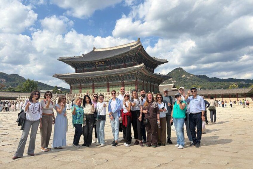 A group of people posing in front of a traditional Korean building with a tiled roof and a stone base. 5