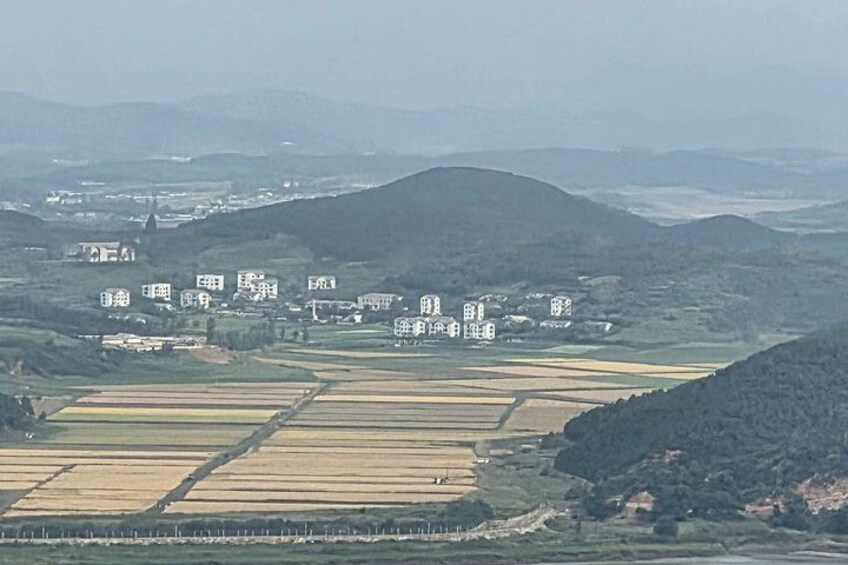 A rural landscape with fields, a village, and hills in the background. 2