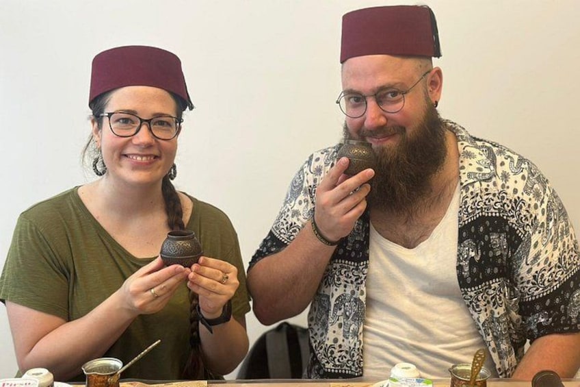 Twee personen zitten aan een tafel met een klein pannetje en een lepel. 5