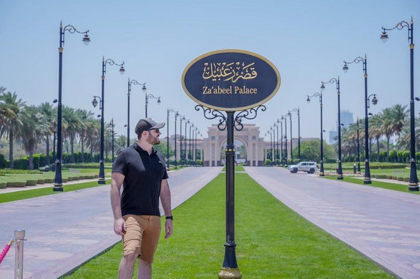 A man walking on a pathway with a sign reading 'Za'abeel Palace' in the background. 4