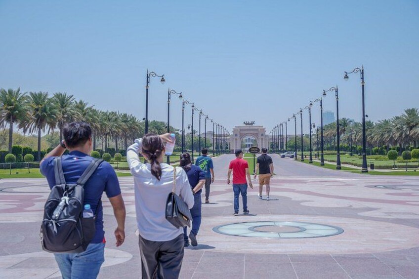 A group of people walking in a park with a fountain and palm trees. 2