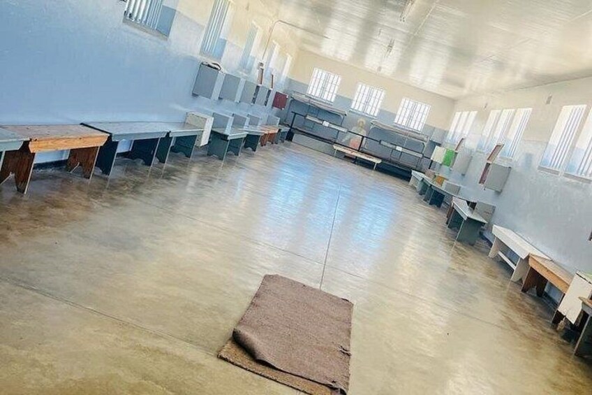A large, empty classroom with rows of desks and chairs, a wooden bench, and a carpet on the floor. 4