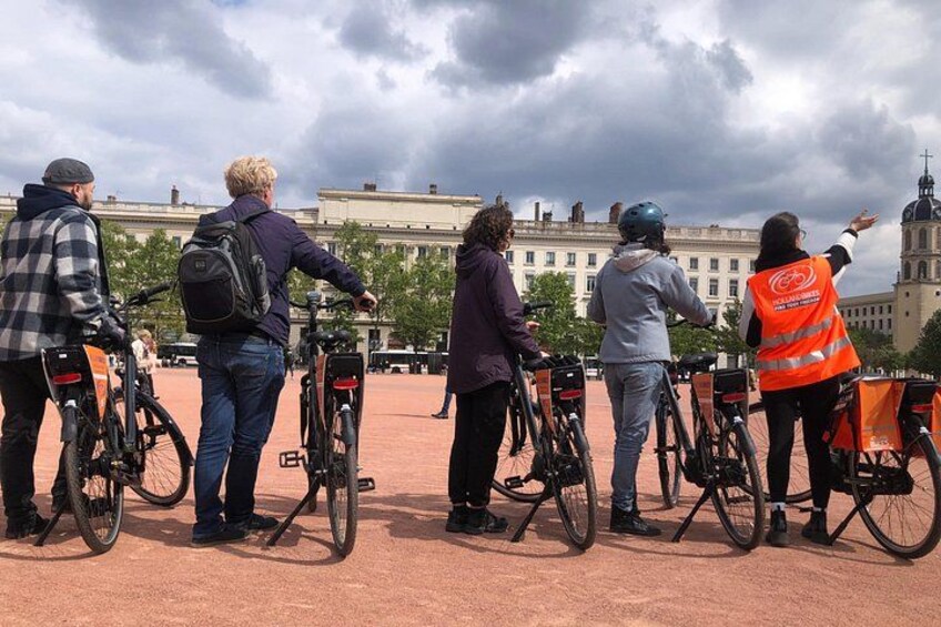 Een groep mensen met fietsen, een historisch gebouw en een bewolkte lucht. 4