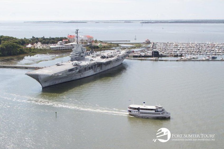A large naval ship docked at a port with a smaller boat in the foreground. 2