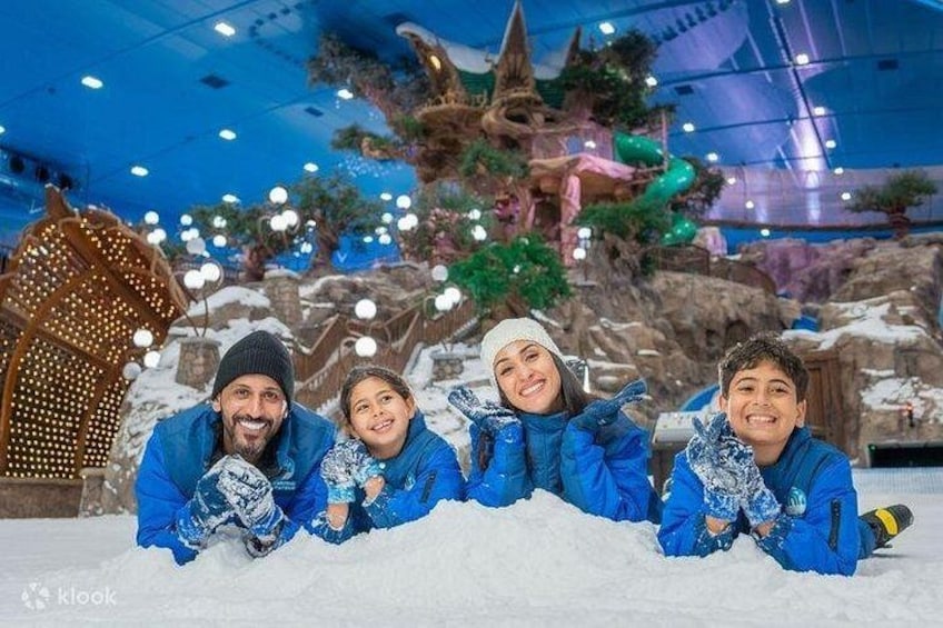 Un gruppo di persone con abiti invernali blu che posano di fronte a un paesaggio innevato, con una grande stella di neve illuminata e un albero sullo sfondo. 1