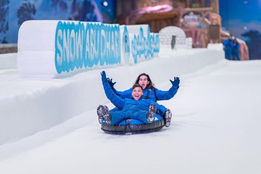 Due persone sciano su una pista innevata, con un cartello che recita 'SNOW ABU DHABI' sullo sfondo. 5