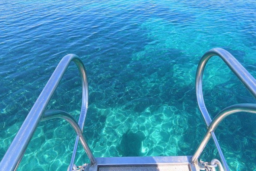 Una scala metallica di una barca che si immerge in acqua cristallina blu. 2