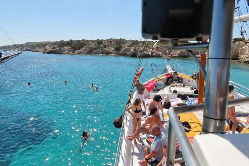 Una barca con persone che nuotano, una costa rocciosa e un cielo sereno. 3