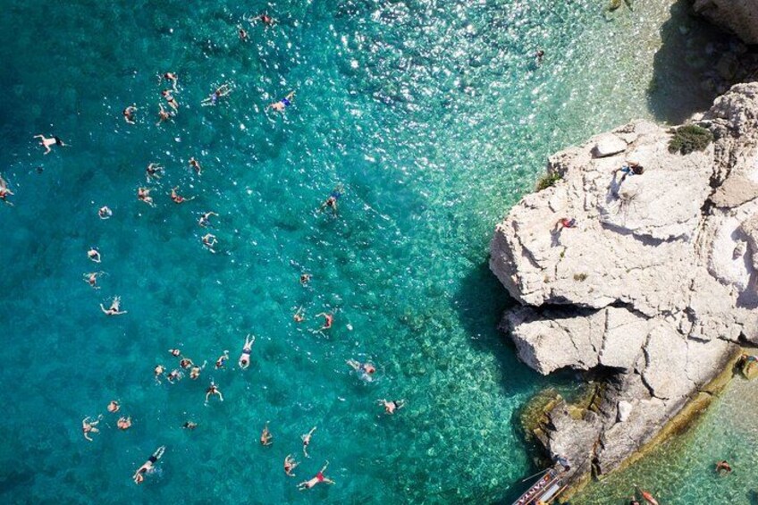 Une zone côtière caractérisée par une eau turquoise et limpide, des formations rocheuses et des personnes qui se baignent. 3