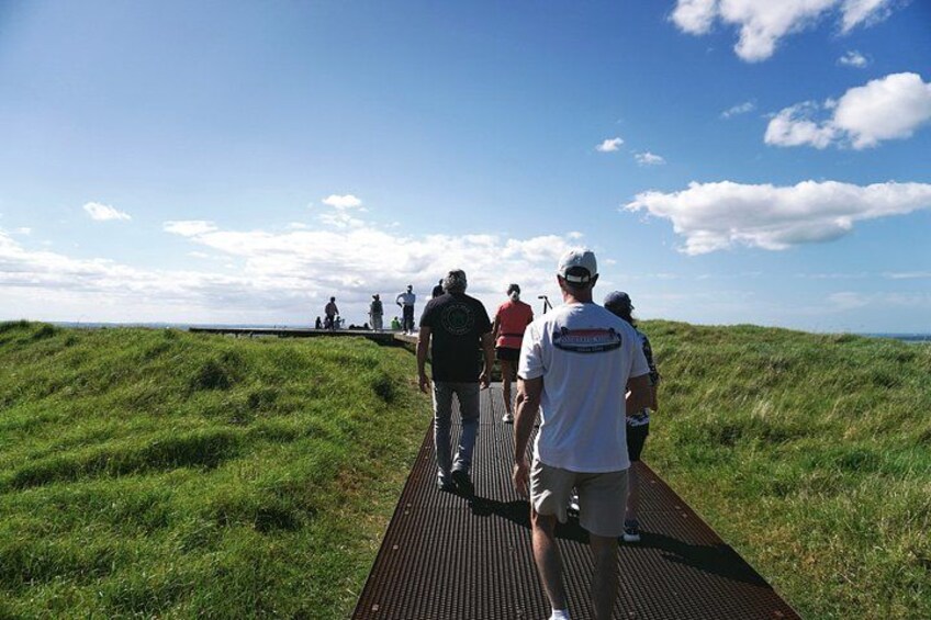 Een groep mensen loopt over een houten looppad door een grasachtig landschap. 2