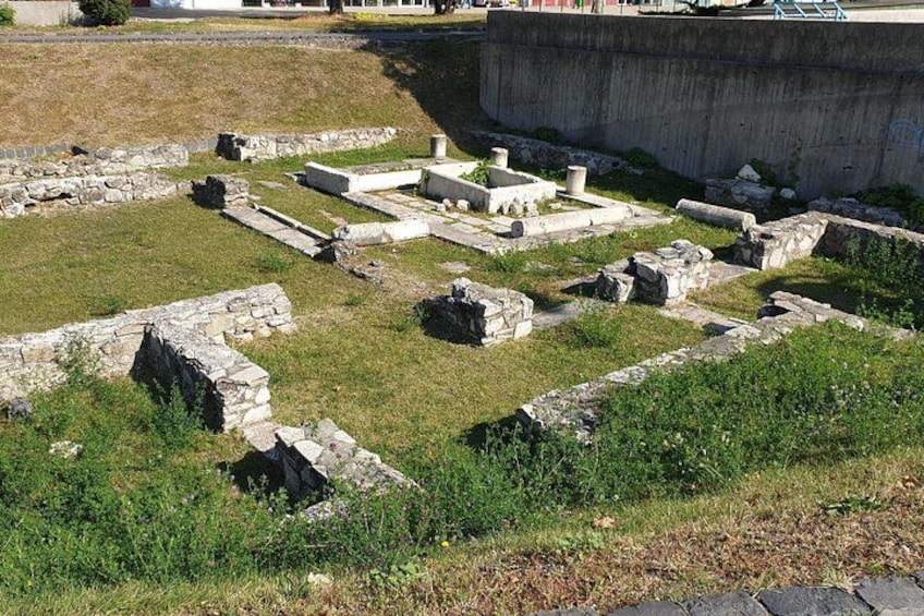Oude ruïnes met stenen constructies en muren, omgeven door gras en een betonnen afscheiding. 2