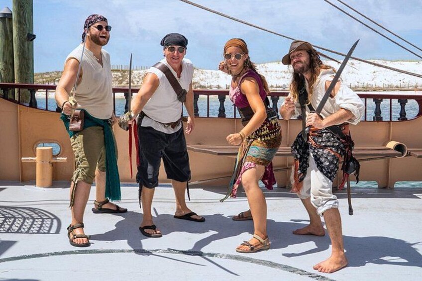 Un grupo de personas en la cubierta de un barco, algunas empuñando espadas y vistiendo trajes de época. 3