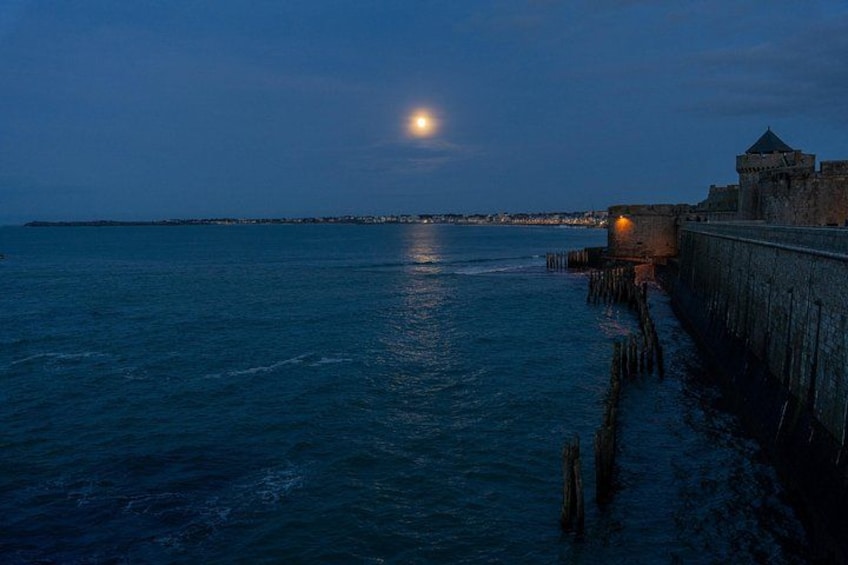 Une scène côtière nocturne, avec un ciel illuminé par la lune, une mer calme et une fortification historique. 5