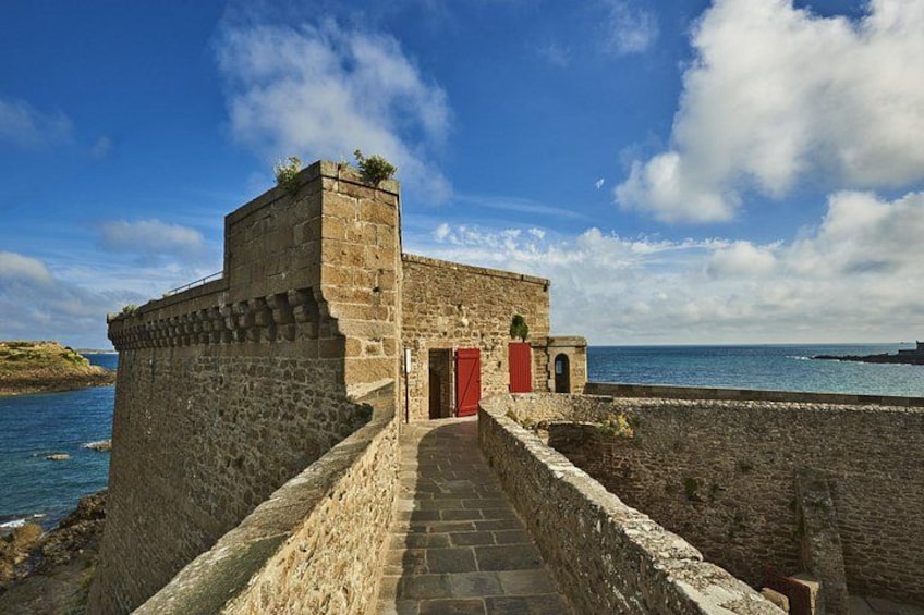 Une fortification en pierre avec une porte rouge, un escalier en pierre et une vue sur la mer. 3