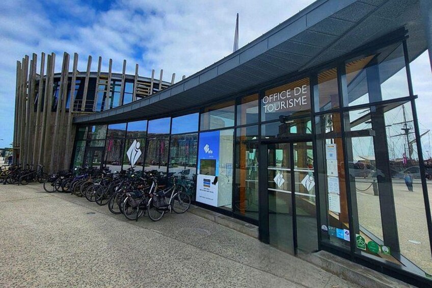 Un bâtiment moderne avec une enseigne indiquant « OFFICE DE TOURISME » et une rangée de vélos garés à l’extérieur. 4