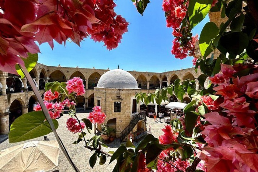 Ein Innenhof mit Kuppel, Bögen und blühenden rosa Blumen. 1