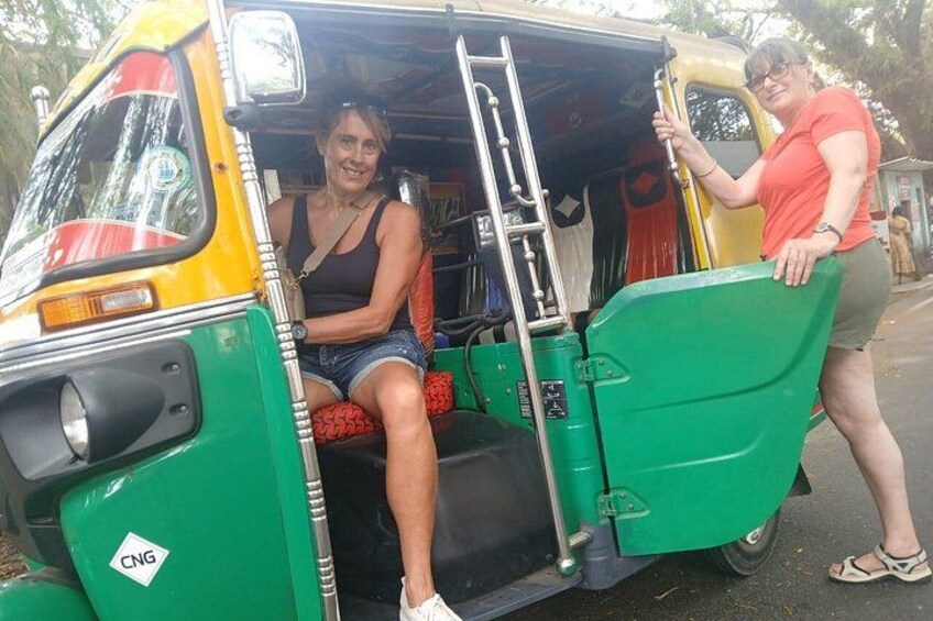 A green auto-rickshaw with a ladder, a person sitting inside, and another person standing outside. 4