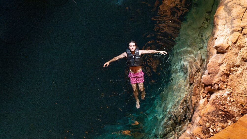 Eine Person schwimmt in einem klaren, blauen Pool, umgeben von Felsen. 1