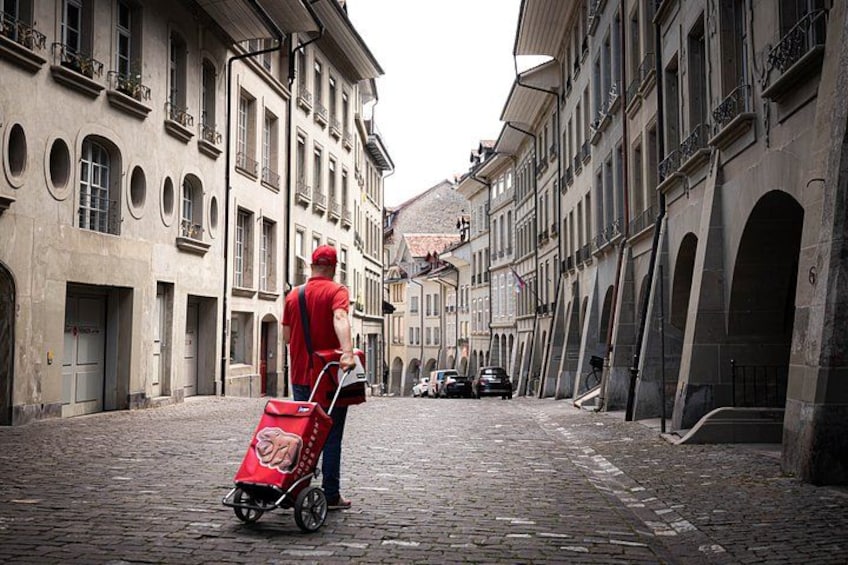 Una persona con camisa roja empujando una maleta roja sobre una calle adoquinada con edificios históricos. 5