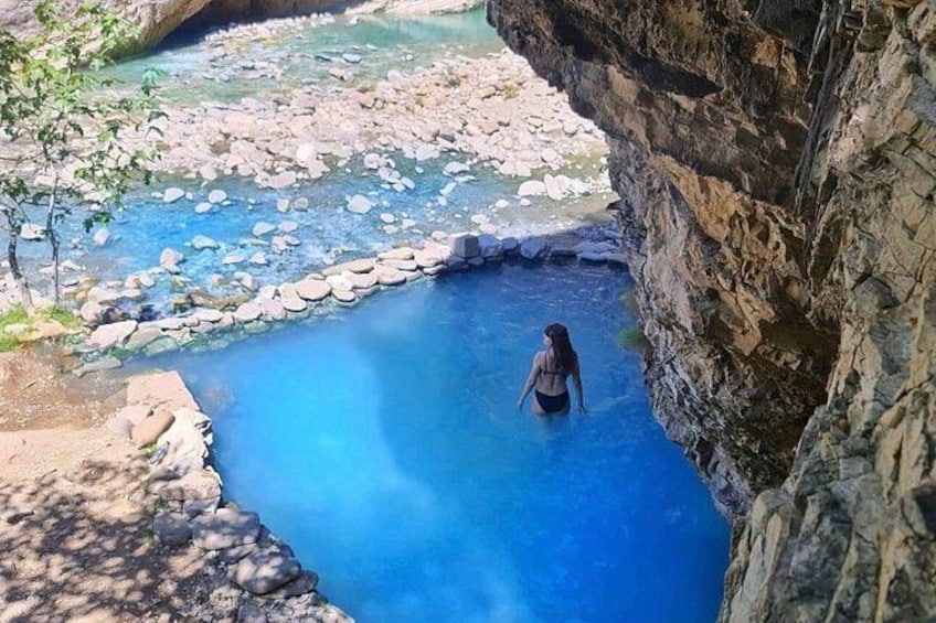 Une personne se tient debout dans une piscine à l’eau cristalline, entourée de falaises rocheuses. 1