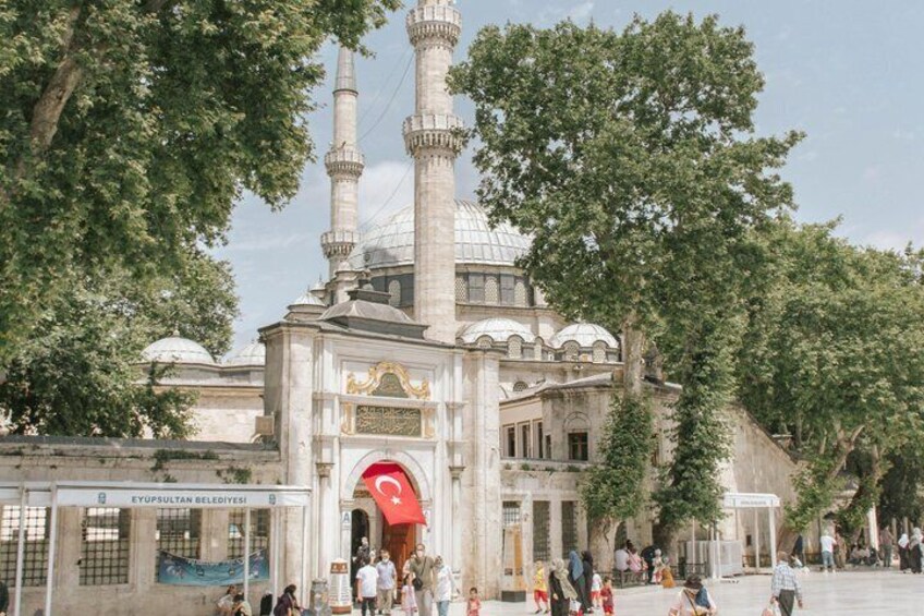 A historic building with two minarets, a large dome, and a red flag. 5