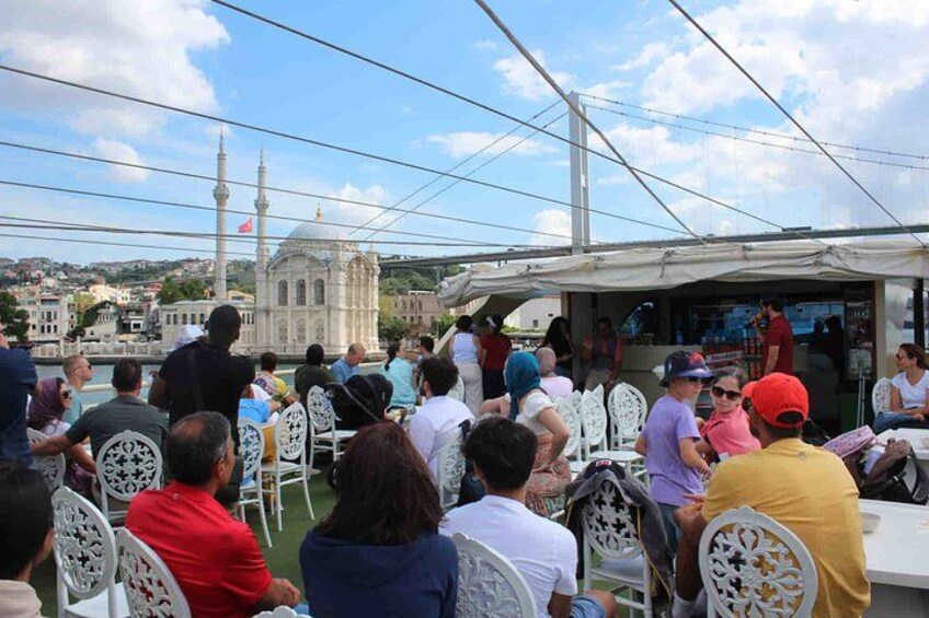 A group of people seated at tables under a tent, with a mosque and cityscape in the background. 3