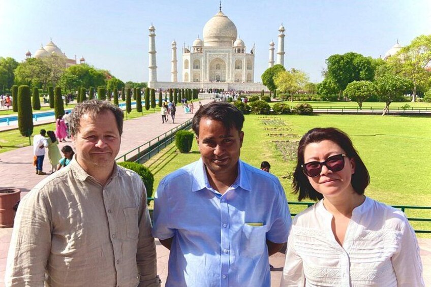 Tres personas frente al Taj Mahal, con un jardín cuidado y cielo despejado. 2