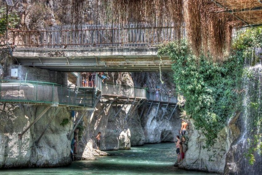 A bridge over a river with people walking on it and a waterfall in the background. 5