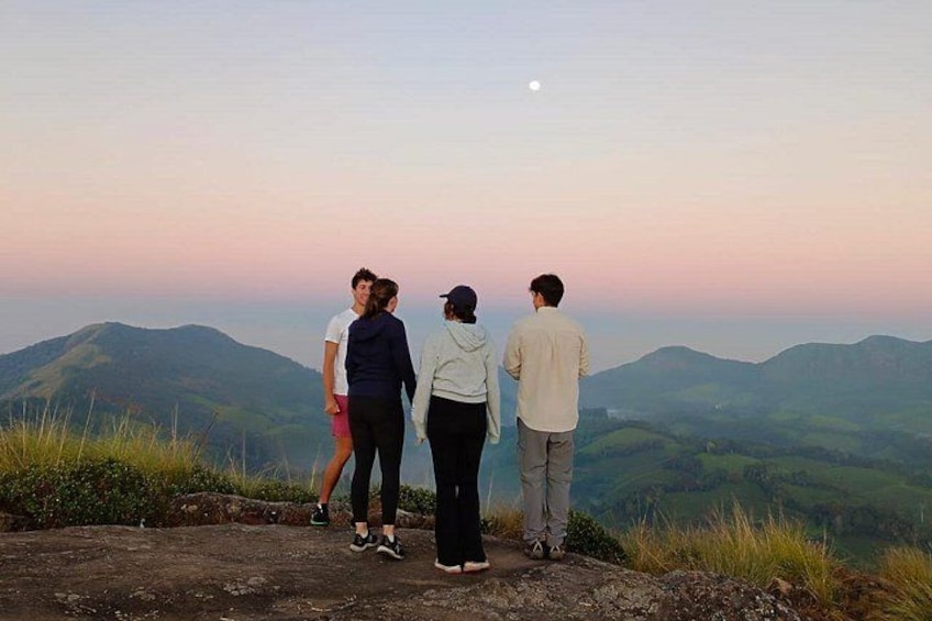 Four people standing on a rocky outcrop overlooking a mountainous landscape during twilight. 4