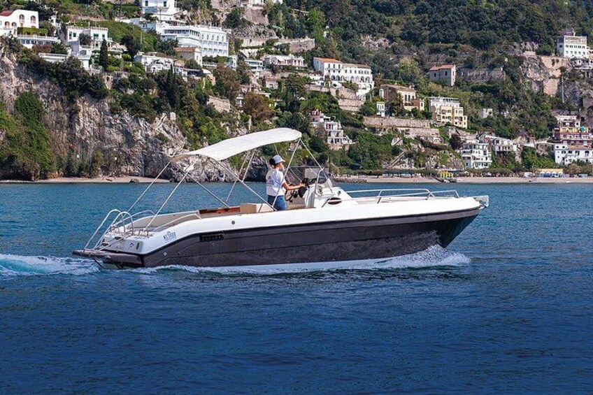 Un bateau à moteur doté d’une cabine, naviguant sur une eau calme, avec une ville côtière en arrière-plan. 3