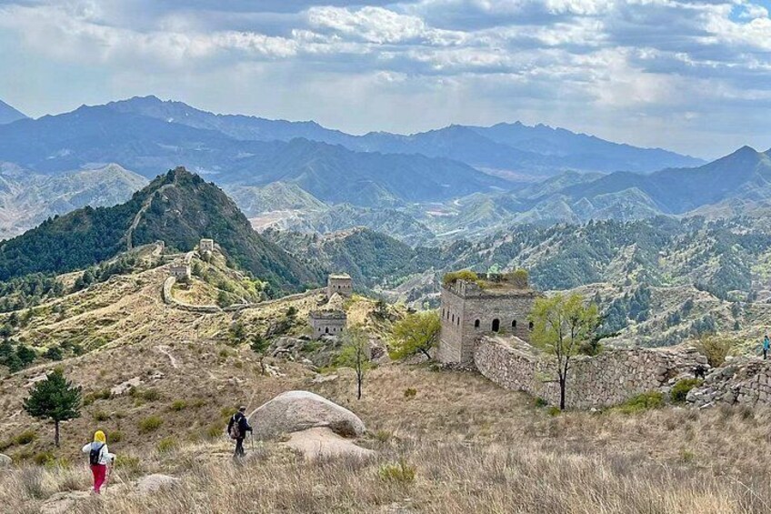 A mountainous landscape with ancient ruins, including a watchtower and a wall, under a partly cloudy sky. 3