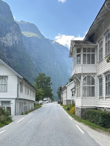 A mountain road flanked by white buildings with large windows and a stone wall. 5