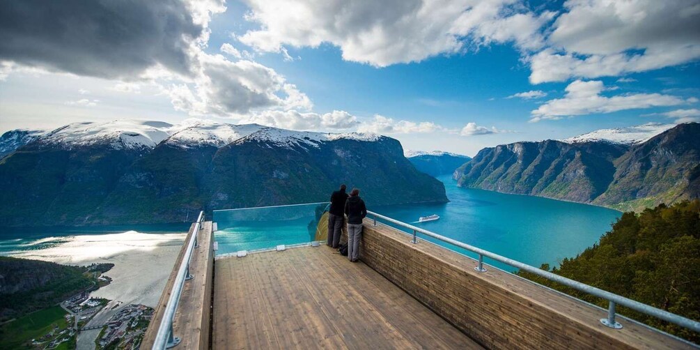 A wooden viewing platform overlooking a fjord with mountains and a clear sky. 1