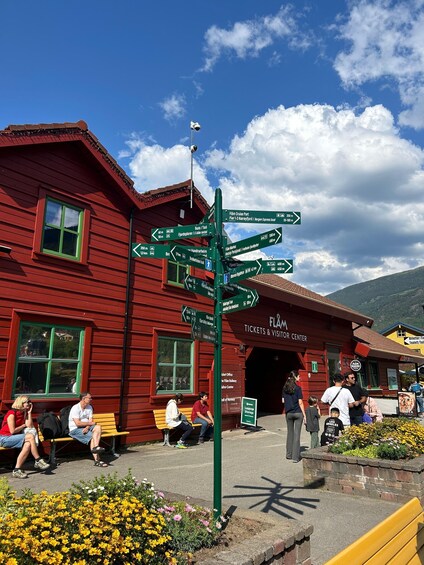 A red building with a signpost, benches, and people sitting outside. 3