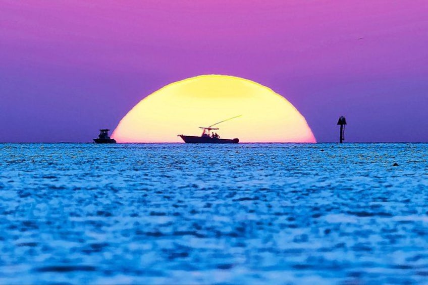 Een zonsondergang boven de oceaan, met een bootje en een vuurtoren in de verte. 1