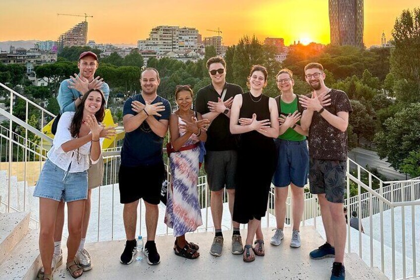 Een groep mensen staat op een balkon met een zonsondergang op de achtergrond. 1