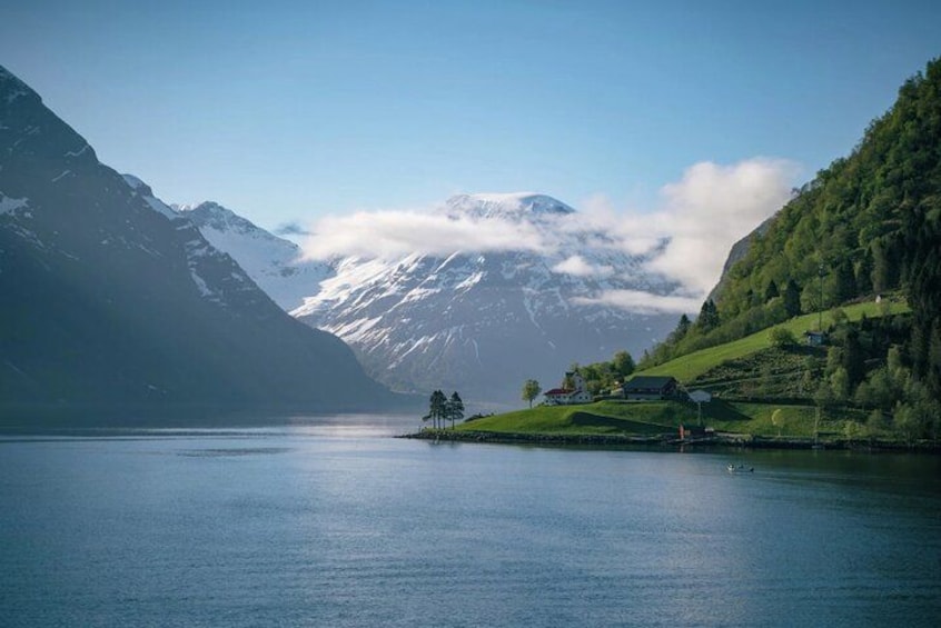 A calm lake surrounded by mountains, a small island with a house, and a clear sky. 1