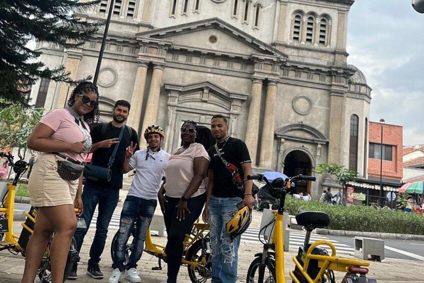 A group of people standing in front of a large building with columns and a clock. There are bicycles parked nearby. 4