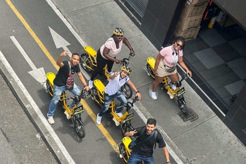 People riding yellow scooters on a city street. 5