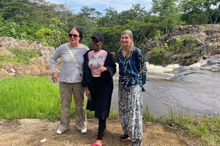 Tres personas de pie junto a un río, con vegetación y rocas al fondo. 4