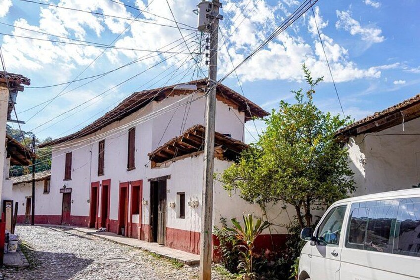 A white building with red accents, a cobblestone street, a parked white car, and a tree. 2