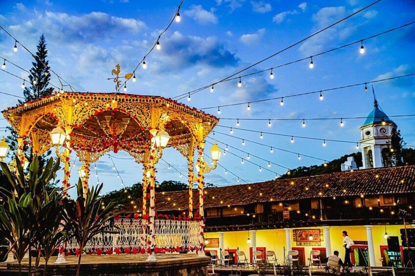 A gazebo with intricate designs, a clock tower, and a building with a tiled roof. 1