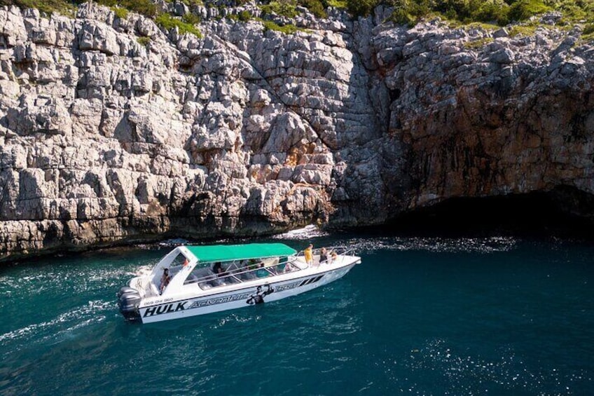 A boat named "Hulk" with a green canopy, sailing near rocky cliffs. 1